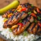 Grilled Huli Huli chicken with glossy pineapple-soy glaze, sliced and served over white rice with grilled pineapple and chopped green onions.