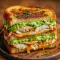 Toasted sandwich filled with sliced grilled chicken, ripe avocado, melted cheese and tomato, halved and stacked on a wooden board.