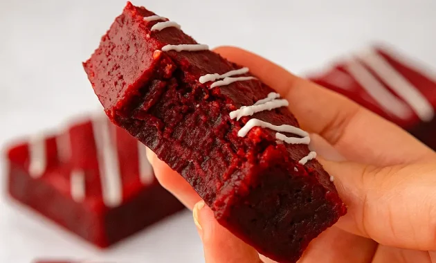 Stack of fudgy red velvet brownie squares with a crackly top, dusted with powdered sugar and drizzled with white chocolate — a cozy autumn treat.