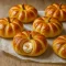 Tray of golden crescent pumpkins filled with cream cheese and spiced pumpkin filling, topped with pretzel stems and a dusting of cinnamon.
