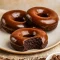 Close-up of three glazed chocolate protein donuts on parchment with almond crumbs — a perfect visual for Healthy Sweet Protein Snacks, and a tempting idea for a Protein Air Fryer Dessert. This shot also reads as Gluten Free Paleo Desserts and Healthy Non Dairy Desserts, with a decadent Health Chocolate Desserts vibe; great for Dairy Free Healthy Meals, Healthy Gluten Free Baking Recipes, labeled as Macros Desserts and useful inspiration for Protein Powder Meals.
