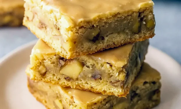 Close-up of a maple-glazed apple blondie square with tender apple bits and a glossy maple drizzle on parchment paper.