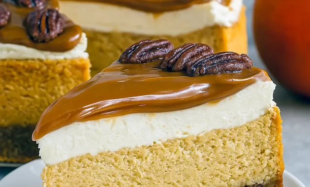 Slice of pecan pie pumpkin cheesecake on a white plate, drizzled with caramel and topped with candied pecans, fork at the side.