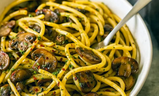 Spaghetti tossed with sautéed mushrooms, garlic, chili flakes, parsley and grated Parmesan in a shallow bowl.