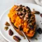 Golden twice-baked sweet potatoes filled with creamy mashed sweet potato and topped with a crunchy pecan streusel, served on a rustic platter.