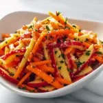 Bowl of crunchy carrot apple salad with shredded carrots, thin apple slices, parsley, and toasted nuts — bright fall side dish.