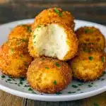 Golden, air-fried mashed potato balls with gooey cheese centers on a serving plate, garnished with chopped parsley and a small bowl of dipping sauce.
