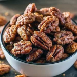 Close-up of golden, gingersnap-coated pecans piled in a jar, showing crunchy spiced coating and scattered sugar crumbs.
