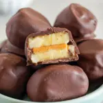 Close-up of chocolate-coated peanut butter banana bites on parchment paper, some sprinkled with crushed chocolate chips and ready straight from the freezer.