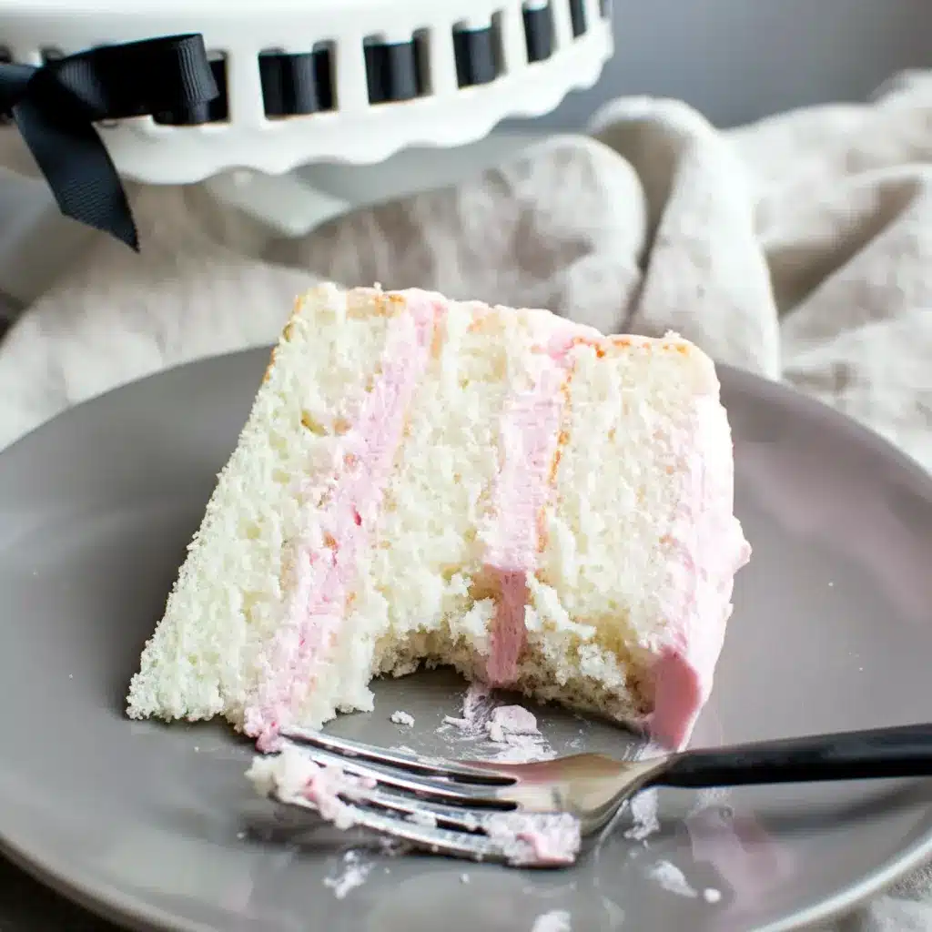 Three-tier white almond layer cake on a white stand, smooth whipped buttercream frosting, a slice removed to reveal the tender, pale crumb, White Almond Cakes.
