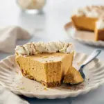 Slice of no-bake marshmallow pumpkin pie in a graham cracker crust, topped with whipped cream and toasted marshmallows, ready for Thanksgiving dessert.