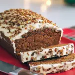 Slice of gingerbread loaf with cream-cheese frosting and chopped pecans on a wooden board — warm, spiced holiday bread.