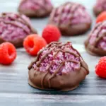 Close-up of chocolate-dipped raspberry coconut macaroons on parchment paper, golden edges and shiny chocolate coating, Easy Christmas Cookie Recipes.