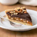 Close-up of a slice of Chocolate Turtle Pie showing glossy chocolate ganache, a brown-sugar caramel layer and a pecan-cookie crust.