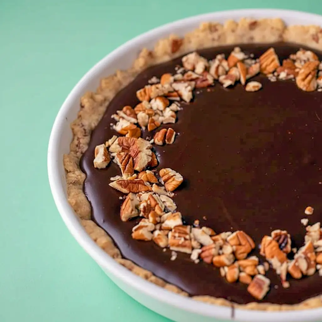Close-up of a slice of Chocolate Turtle Pie showing glossy chocolate ganache, a brown-sugar caramel layer and a pecan-cookie crust.