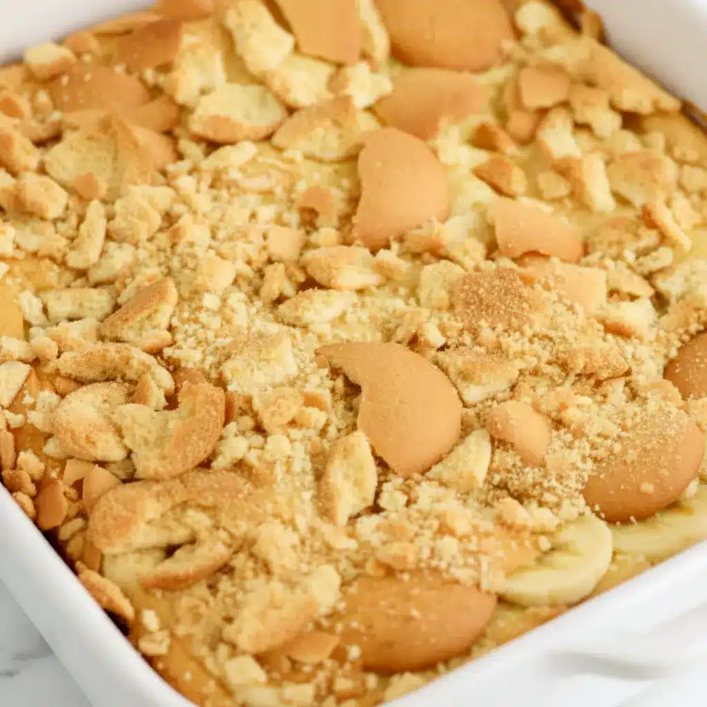 Golden banana blondie squares topped with sliced bananas and crushed vanilla wafers on a serving plate, Banana Pudding Brownie.