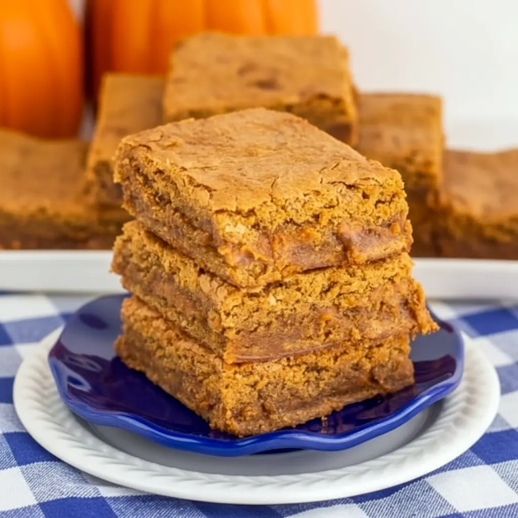 Close-up of a stack of chewy, golden pumpkin blondies with visible cinnamon chips and a glossy top — photo represents the Pumpkin Blondies Recipe, a mash-up alternative to Pumpkin Brownies, highlighting Pumpkin Spice Blondies, Pumpkin Pie Spice Blondies, and Pumpkin Blondies With Cinnamon Chips; suggests the simple Pumpkin Spice Blondie Recipe With Pumpkin Puree for easy Halloween Blondies, styled like a classic Blondies Recipe and featured in Pumpkin Recipes Dessert.
