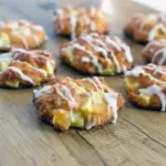 Close-up of a glazed keto apple fritter cookies sprinkled with cinnamon sugar and tiny apple pieces on a cooling rack.