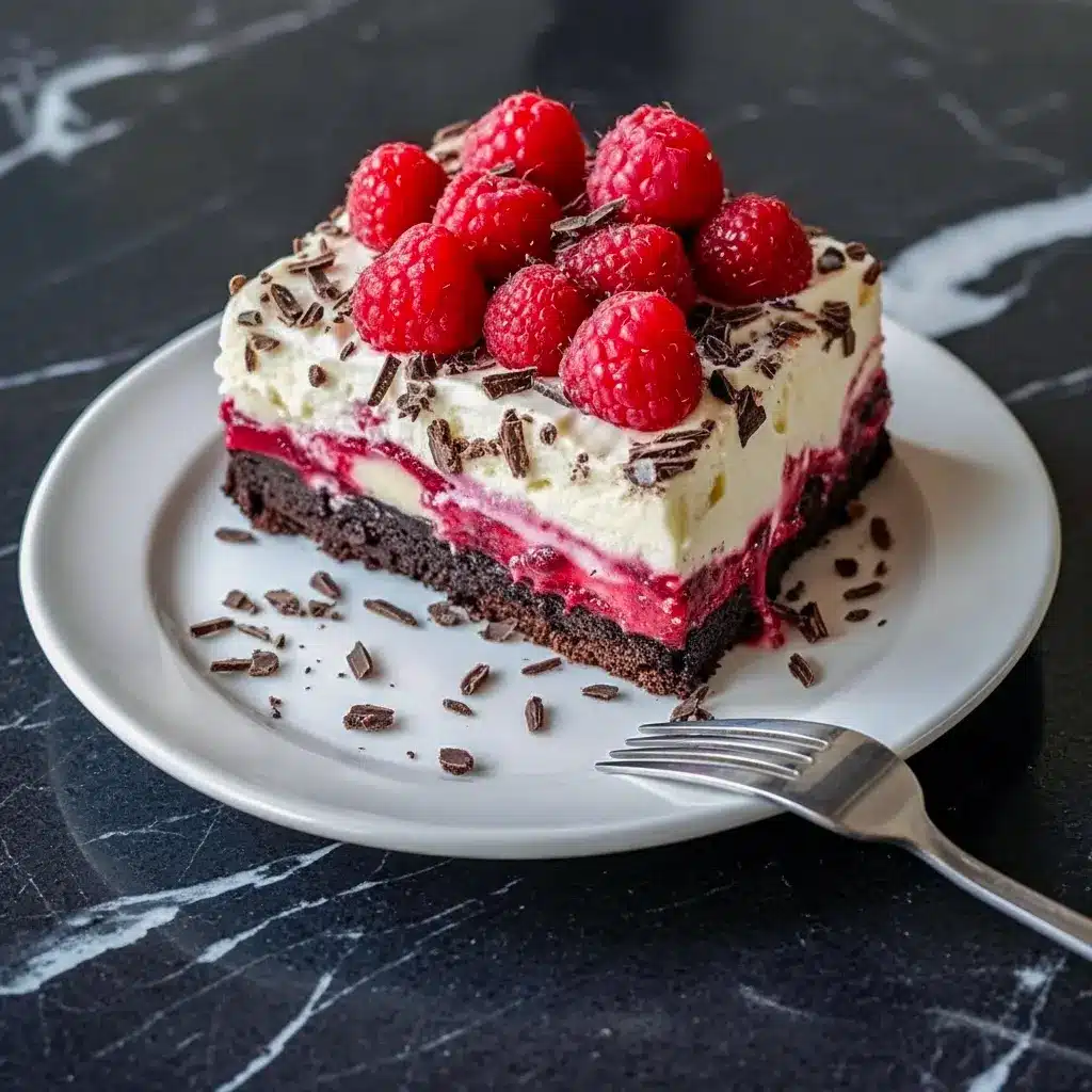 Close-up of a slice of raspberry chocolate lasagna showing a chocolate cookie crust, a dark chocolate pudding layer, a pink raspberry-cream layer, whipped topping, fresh raspberries, and chocolate shavings on a dessert plate, Raspberry Layered Dessert.