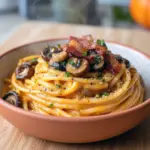 Fall Spaghetti Recipes — creamy pumpkin pasta with sautéed mushrooms and crispy bacon on a white plate, garnished with parsley and grated Parmesan.