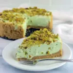 Slice of creamy Pistachio Cheesecake with whipped topping and crushed pistachios on a plate — the perfect Easy Pistachio Dessert for pistachio lovers.