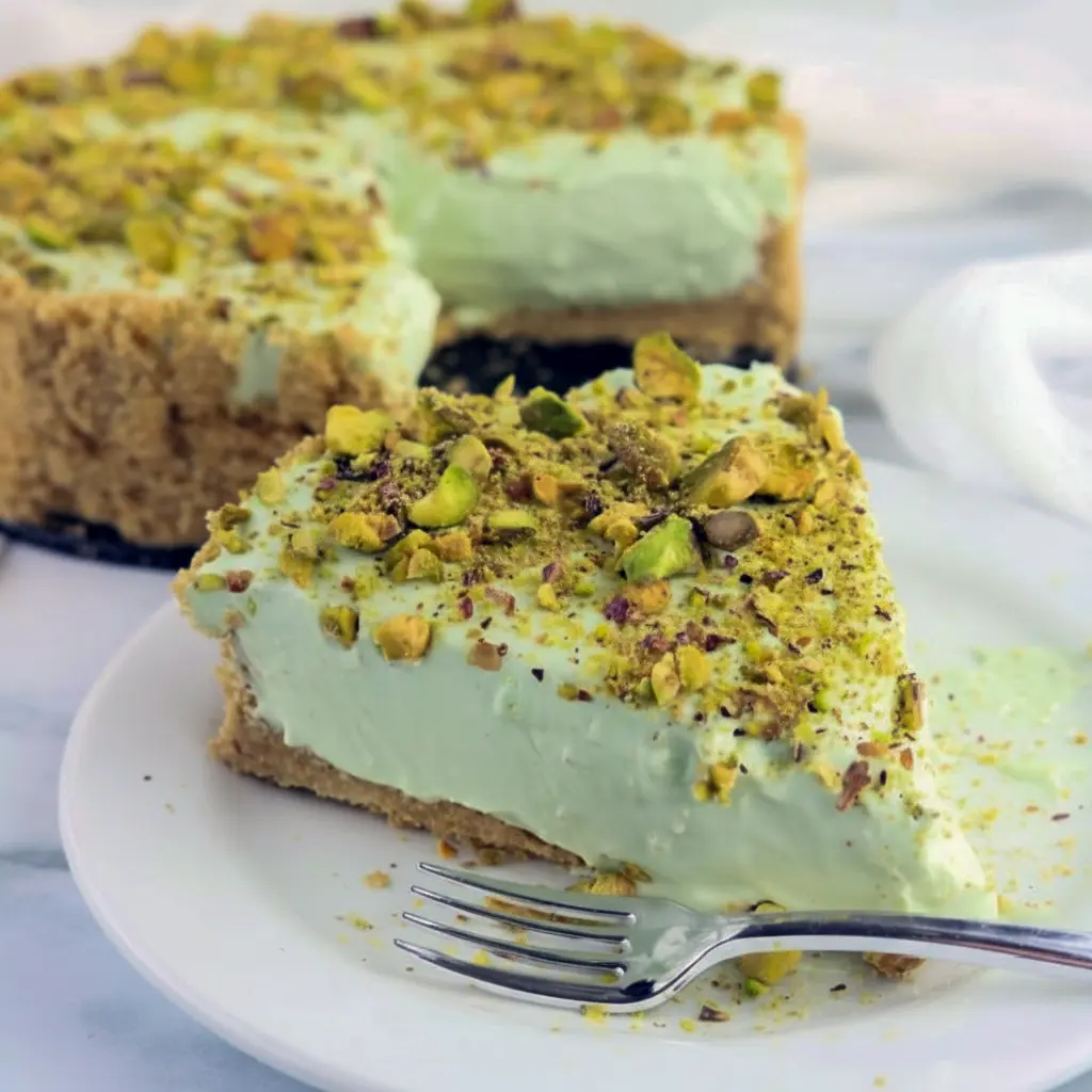 Slice of creamy Pistachio Cheesecake with whipped topping and crushed pistachios on a plate — the perfect Easy Pistachio Dessert for pistachio lovers.