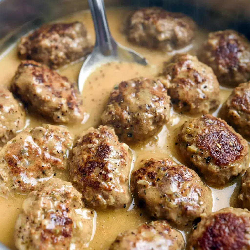 Close-up of golden, lemon-glazed keftedes on a platter with lemon wedges and herbs — Tasty Meatballs Recipe.
