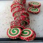 Close-up of red-and-green swirled pinwheel cookies stacked on a ceramic plate with holiday ribbon and sprinkles, Christmas Sweets.