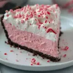 Slice of no-bake peppermint pie in a chocolate cookie crust, topped with whipped cream and crushed candy cane, on a festive holiday plate, Easy Baking Christmas.