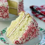 Slice of peppermint layer cake with white buttercream, crushed candy-cane rim, and a sprig of evergreen on a festive plate, Peppermint Cake.