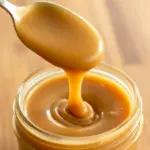 Keto Salted Caramel spoon pouring into a jar, glossy and thick; caption notes Low Carb Keto Caramel Sauce Recipe, nearby are bite-size Keto Caramel Fat Bomb Recipe squares and a dish labeled Keto Candy; the photo sits among jars labeled Keto Sauces and a stack of Breakfast Low Carb pancakes, suggesting easy Keto Dessert Easy and other Low Carb Sweets for Joy Filled Eats.