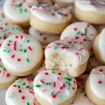 Close-up of frosted peppermint meltaway cookies dusted with crushed candy cane, stacked on a festive plate.