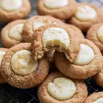 Cinnamon-sugar snickerdoodle thumbprint cookies filled with creamy white eggnog ganache and topped with grated nutmeg on a cooling rack, The Best Holiday Cookies.