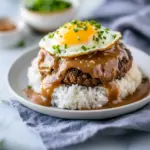 Plate with rice, a seared patty drenched in brown gravy and a fried egg on top — perfect for Ground Beef Recipes, a standout among Interesting Food Recipes, ideal for hearty Meat Recipes, and utterly Satisfying Food, Hawaiian Dishes.