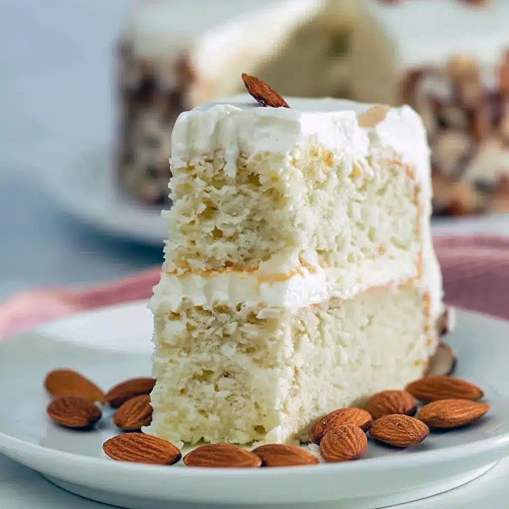 Best Ever Almond Cream Cake slice with whipped almond frosting and toasted sliced almonds, styled on a white plate.