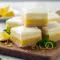 Lemon Cheesecake bar sliced on parchment, showing a creamy lemon layer over a cheesecake topping and golden crust, dusted with powdered sugar — elegant Cheesecake Bar ready to serve.