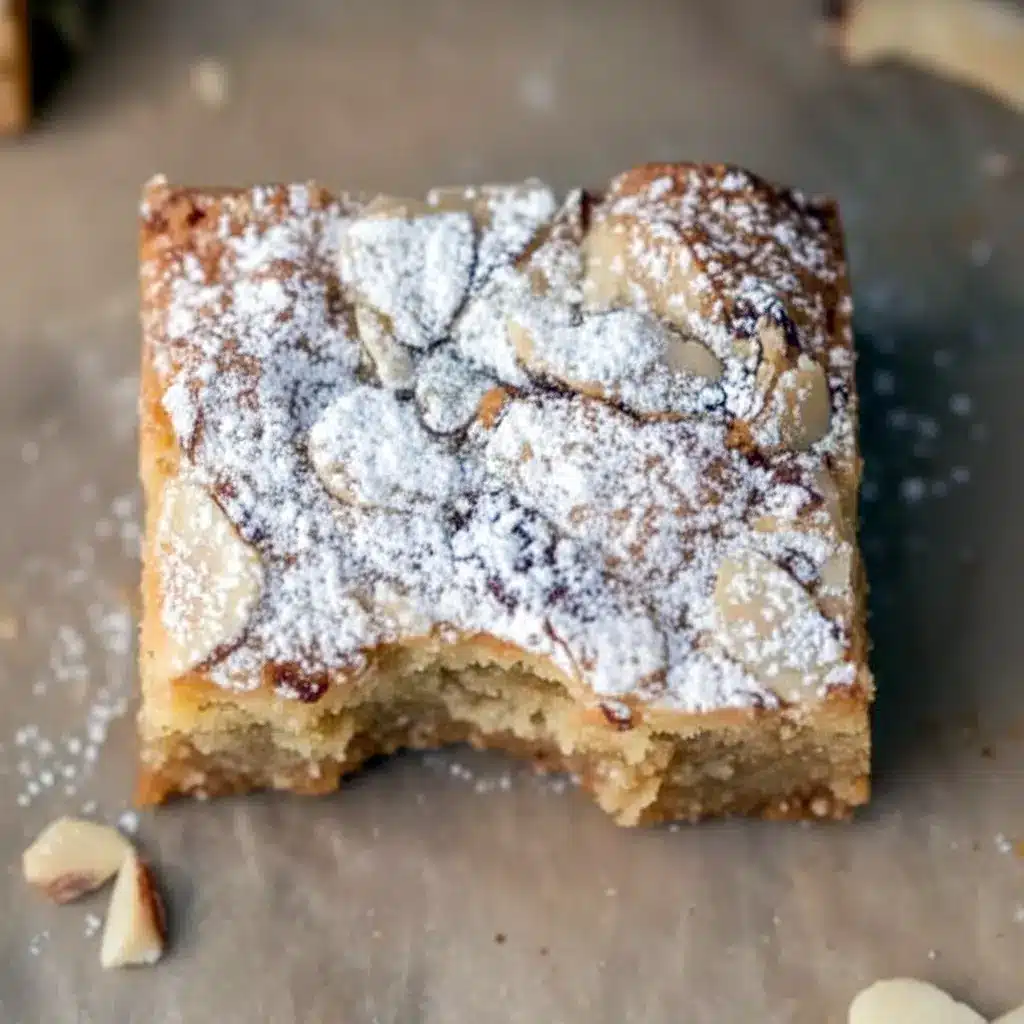 Close-up of golden blondie squares with swirled almond frangipane, toasted sliced almonds, and a light dusting of powdered sugar, Almond Croissant.