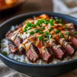 Close-up of a bowl with thinly sliced marinated steak over steamed rice, sautéed bell peppers and broccoli, drizzled with a spicy cream sauce and finished with sesame seeds and chopped green onions, Korean Bbq.
