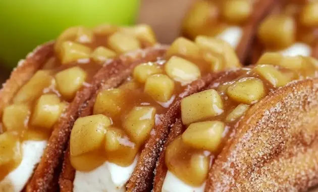 Homemade Apple Cheesecake Tacos: close-up of Cinnamon Sugar Tortillas shaped into taco shells, filled with creamy cheesecake and spiced apple topping, dusted with powdered sugar.