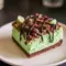 Slice of Mint Chocolate Cheesecake bar on a plate — vivid green mint cheesecake layer over a chocolate crumb crust, drizzled chocolate, and festive sprinkles for Saint Patrick's Day, a tempting example of elegant Cheesecake Bars.