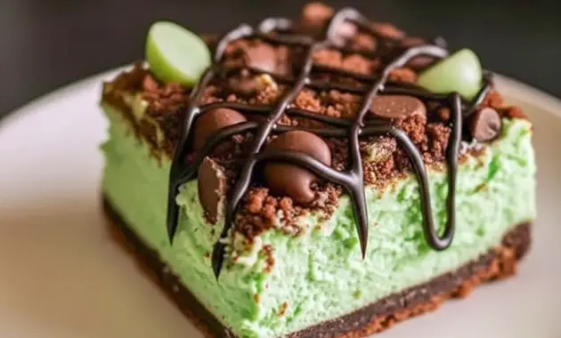 Slice of Mint Chocolate Cheesecake bar on a plate — vivid green mint cheesecake layer over a chocolate crumb crust, drizzled chocolate, and festive sprinkles for Saint Patrick's Day, a tempting example of elegant Cheesecake Bars.