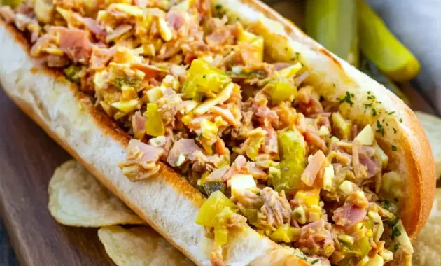 Ultimate Cuban Sandwich halved to show chopped pork, ham, Swiss, dill pickles and mustard inside a toasted garlicky roll.