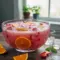 Bowl of icy Slush Punch with citrus slices and a ladle, showing pink, frothy slush and sparkling soda bubbles.