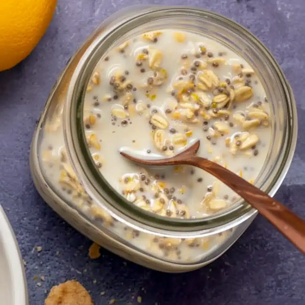 Lemon Cheesecake Overnight Oats in a jar, creamy and pale yellow, topped with lemon zest and fresh berries — a ready-to-eat Creamy Lemon Overnight Oats breakfast.