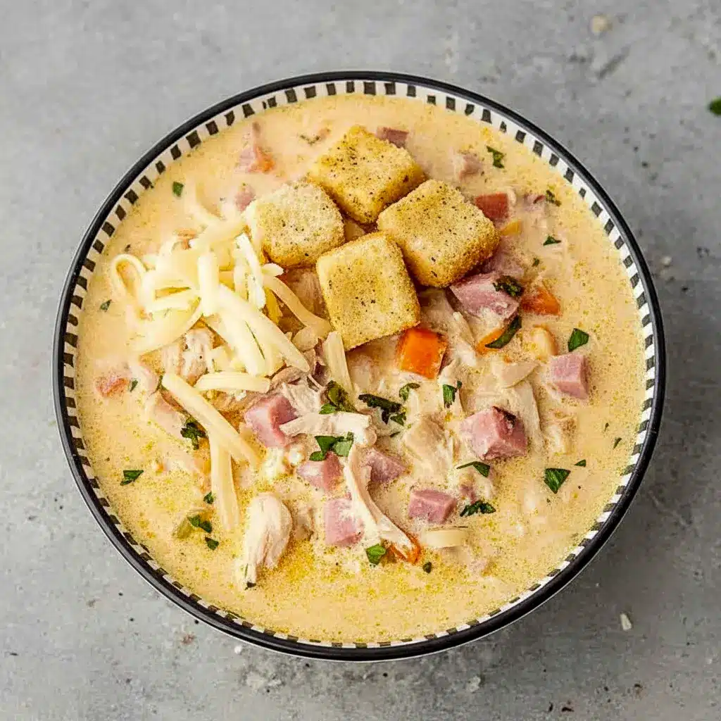 Bowl of Chicken Cordon Bleu Soup with shredded Swiss on top, tender chicken and ham pieces, and a scattering of golden croutons.