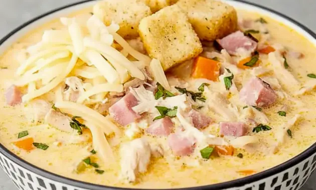 Bowl of Chicken Cordon Bleu Soup with shredded Swiss on top, tender chicken and ham pieces, and a scattering of golden croutons.