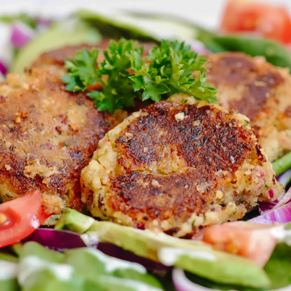 Close-up of golden Easy Falafel Recipe patties on a plate with pita, a bowl of tzatziki, and fresh parsley garnish.