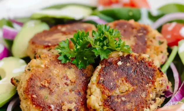 Close-up of golden Easy Falafel Recipe patties on a plate with pita, a bowl of tzatziki, and fresh parsley garnish.