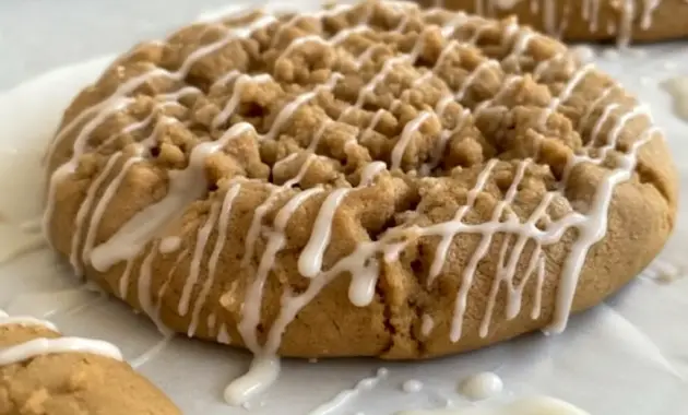 A close-up of Gilmore Girls Coffee Cake Cookies with golden edges, a soft center, cinnamon streusel topping, and vanilla icing, styled like cozy Coffee Cookies on a parchment-lined baking tray.