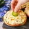 Close-up of baked Jalapeño Popper Bagels — bagel halves spread with jalapeño cream cheese, melted Monterey Jack, and bacon crumbles, garnished with thin jalapeño slices.